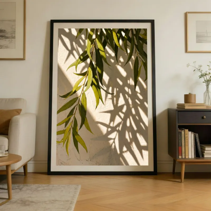 Hanging green willow-like leaves against a textured beige wall with soft leaf shadows cast by sunlight.